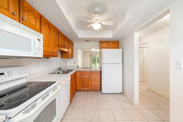 kitchen with white appliances, ceiling fan, light tile flooring, a tray ceiling, and sink