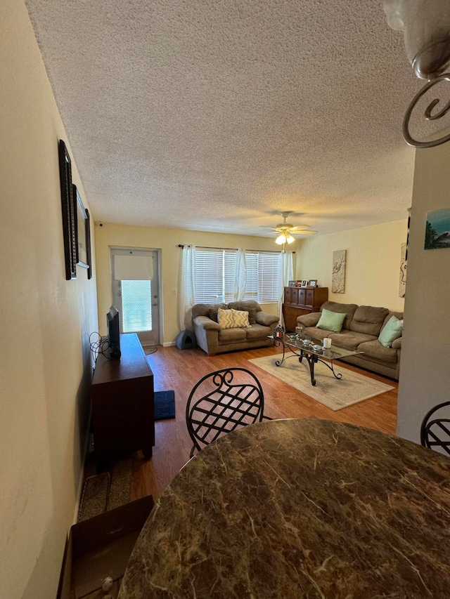 living room with a textured ceiling, wood-type flooring, and ceiling fan