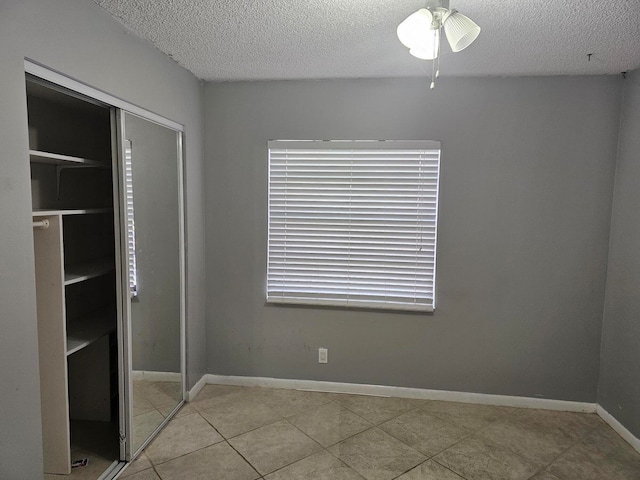 unfurnished bedroom with a closet, a textured ceiling, light tile patterned flooring, and ceiling fan