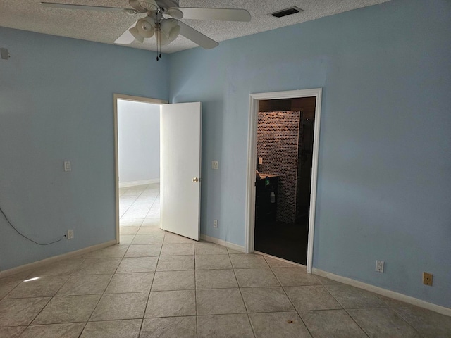 spare room with a textured ceiling, light tile patterned floors, and ceiling fan