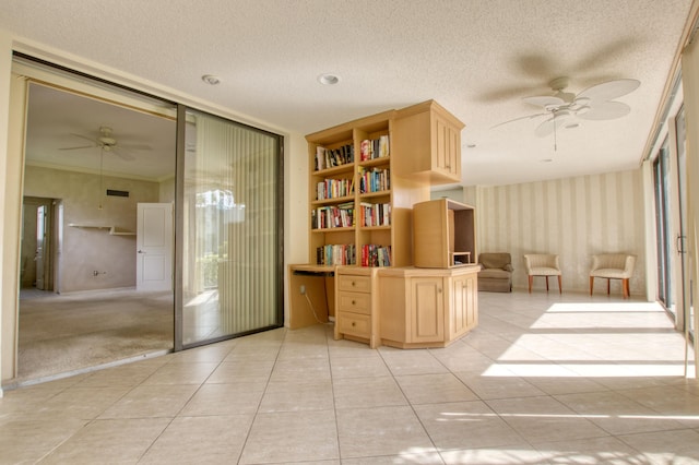 unfurnished office featuring crown molding, built in desk, a textured ceiling, light tile patterned floors, and ceiling fan