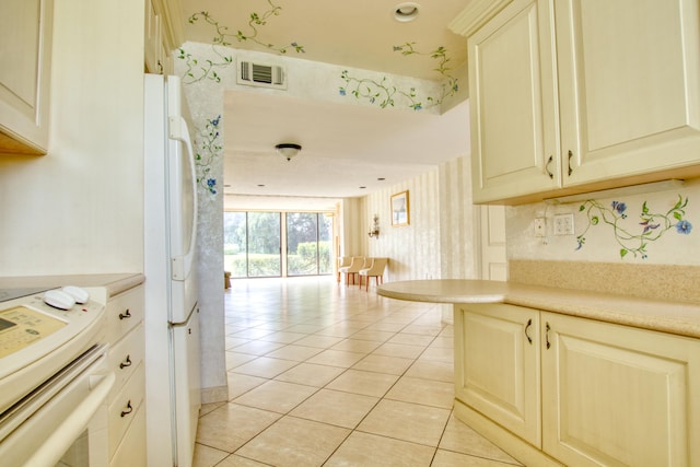 kitchen featuring range, white refrigerator, kitchen peninsula, light tile patterned floors, and cream cabinetry