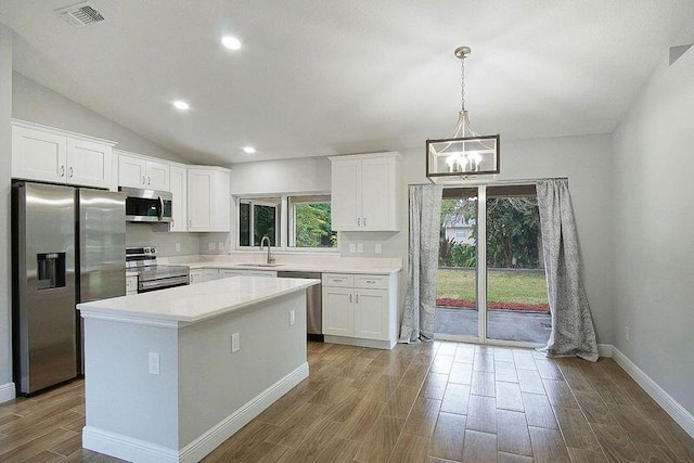 kitchen with hanging light fixtures, stainless steel appliances, a kitchen island, white cabinetry, and sink