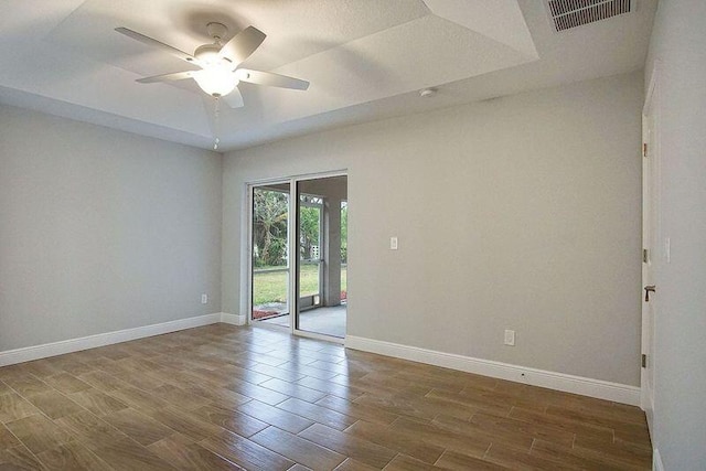 unfurnished room with ceiling fan, a tray ceiling, and dark hardwood / wood-style floors