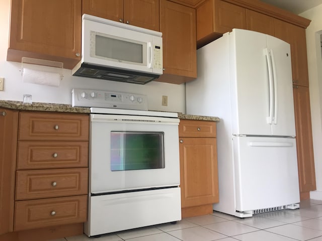 kitchen featuring white appliances, light stone countertops, and light tile flooring