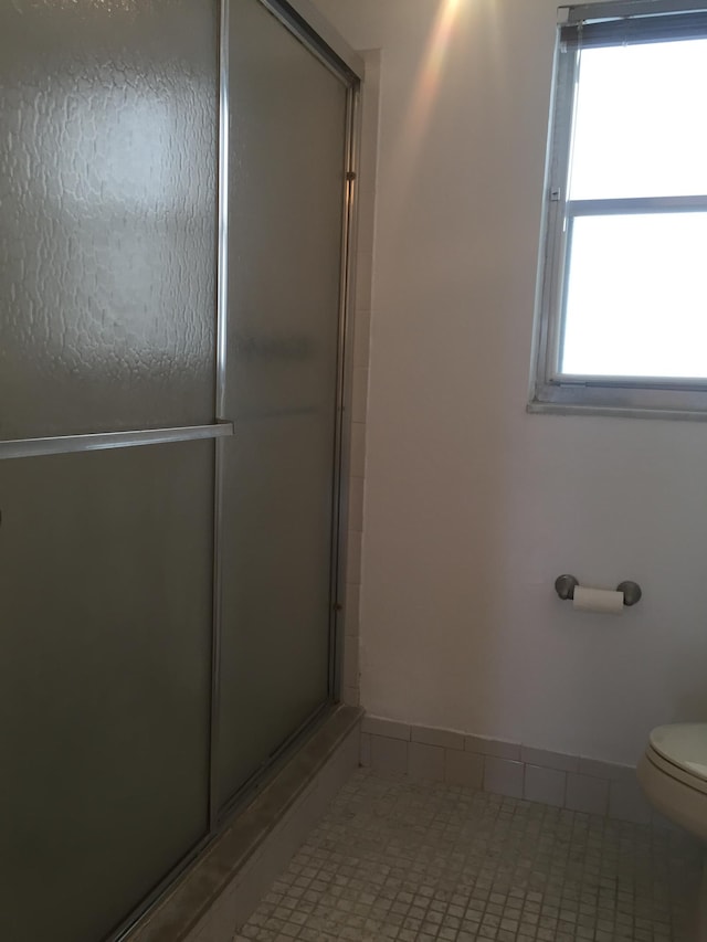 bathroom with tile floors, a shower with shower door, toilet, and a wealth of natural light