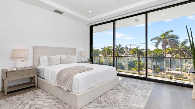 bedroom featuring access to outside, floor to ceiling windows, wood-type flooring, and a water view