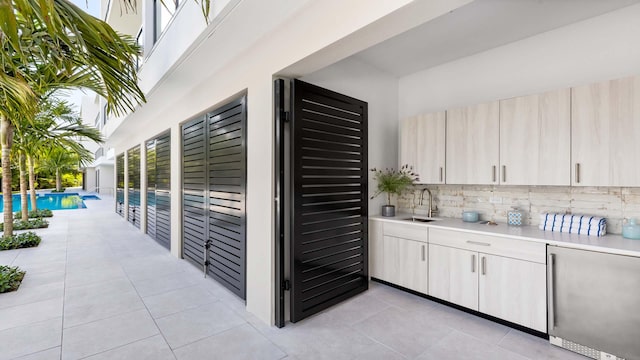 exterior space featuring light brown cabinets, sink, backsplash, and light tile floors