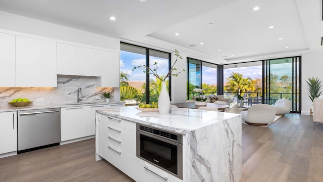 kitchen with stainless steel appliances, a healthy amount of sunlight, tasteful backsplash, wood-type flooring, and white cabinets