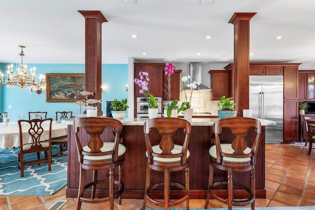 kitchen featuring appliances with stainless steel finishes, backsplash, decorative columns, tile flooring, and wall chimney range hood