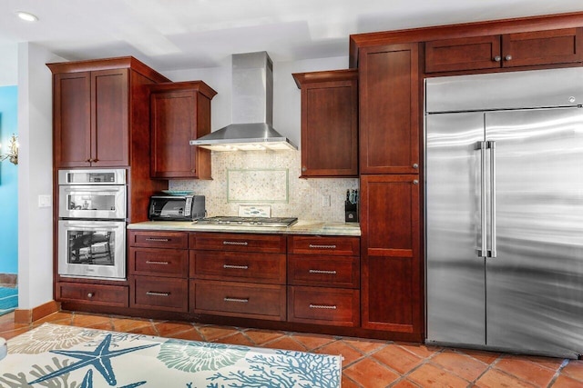 kitchen with wall chimney range hood, stainless steel appliances, light tile floors, light stone counters, and tasteful backsplash