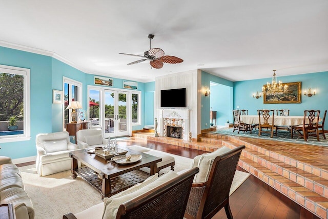 living room with a fireplace, ceiling fan with notable chandelier, crown molding, french doors, and hardwood / wood-style flooring