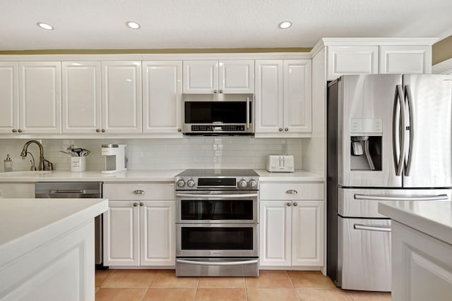 kitchen with white cabinetry, stainless steel appliances, sink, light tile floors, and tasteful backsplash