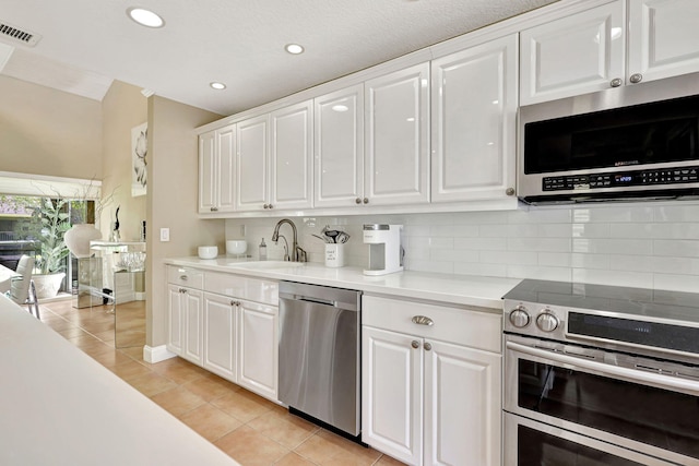 kitchen featuring appliances with stainless steel finishes, tasteful backsplash, white cabinetry, sink, and light tile floors