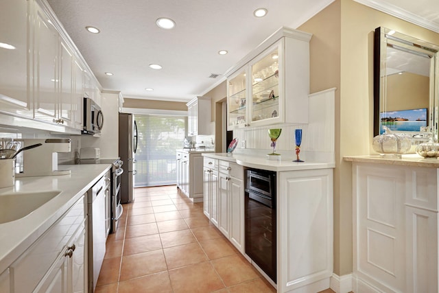 kitchen with beverage cooler, light tile floors, white cabinets, stainless steel appliances, and ornamental molding