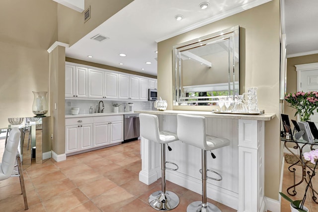 kitchen with backsplash, appliances with stainless steel finishes, light tile flooring, white cabinets, and a breakfast bar