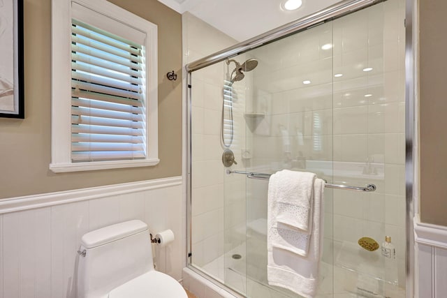 bathroom featuring tile walls, toilet, and a shower with shower door