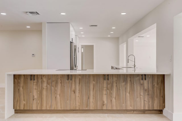 kitchen featuring light tile patterned flooring, kitchen peninsula, sink, and stainless steel refrigerator