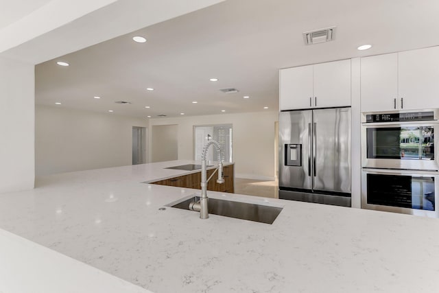 kitchen with white cabinetry, sink, light stone countertops, and stainless steel appliances