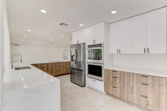 kitchen with light stone countertops, appliances with stainless steel finishes, sink, light brown cabinets, and white cabinetry