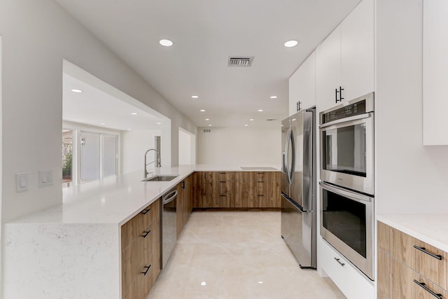 kitchen featuring sink, light stone countertops, appliances with stainless steel finishes, white cabinetry, and kitchen peninsula