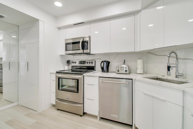 kitchen featuring appliances with stainless steel finishes, light hardwood / wood-style flooring, tasteful backsplash, white cabinets, and sink