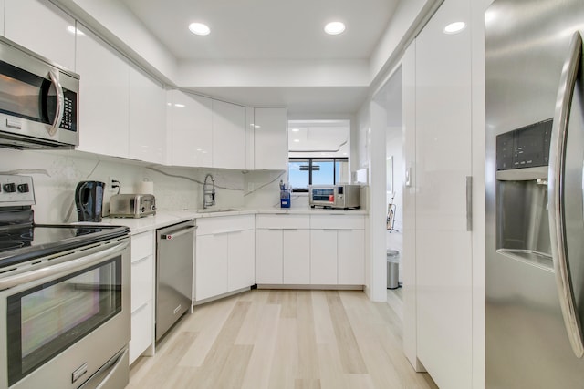 kitchen featuring sink, light hardwood / wood-style floors, backsplash, white cabinetry, and stainless steel appliances