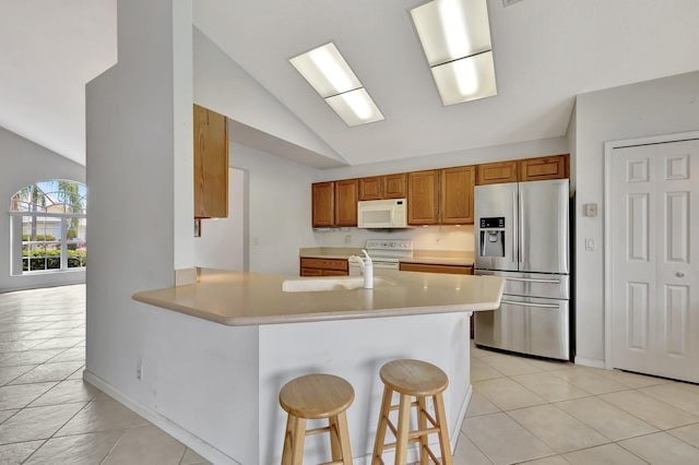 kitchen with light tile floors, a kitchen bar, sink, white appliances, and lofted ceiling