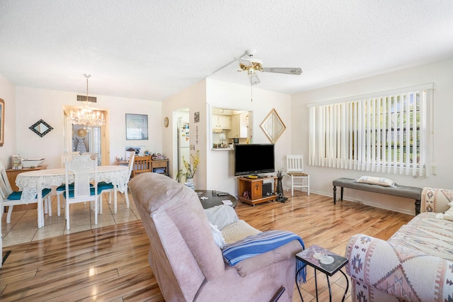 tiled living room with ceiling fan with notable chandelier and a textured ceiling