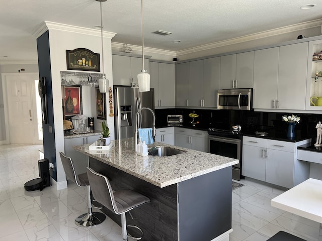 kitchen with a sink, decorative backsplash, a kitchen island with sink, stainless steel appliances, and ornamental molding