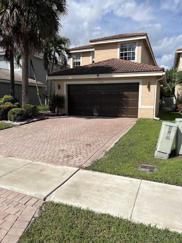 view of front of property with decorative driveway, a tiled roof, an attached garage, a front yard, and stucco siding