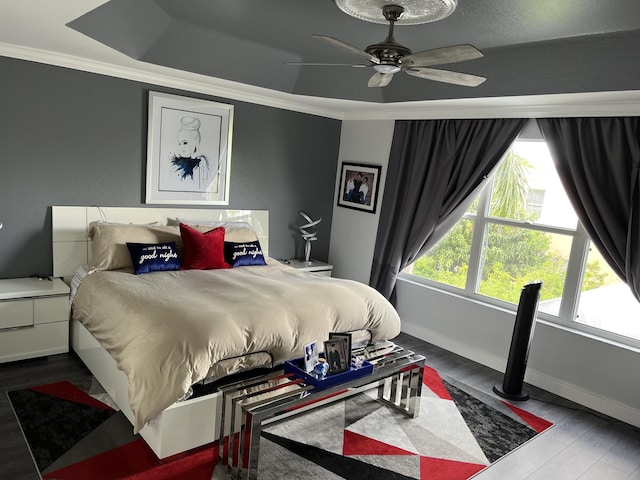 bedroom featuring baseboards, ornamental molding, wood finished floors, and a raised ceiling