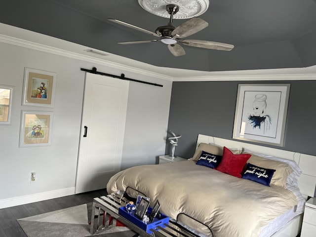 bedroom with a barn door, dark wood-style floors, visible vents, crown molding, and baseboards