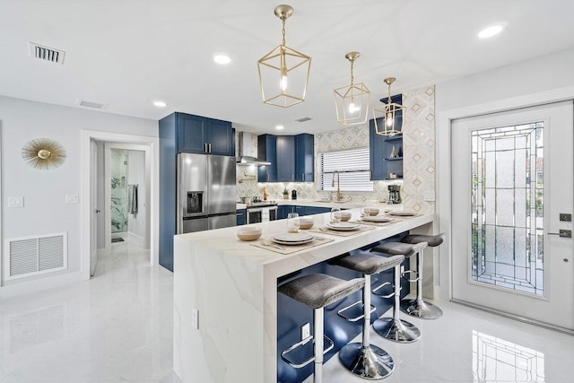 kitchen with blue cabinets, a kitchen breakfast bar, wall chimney range hood, stainless steel appliances, and kitchen peninsula