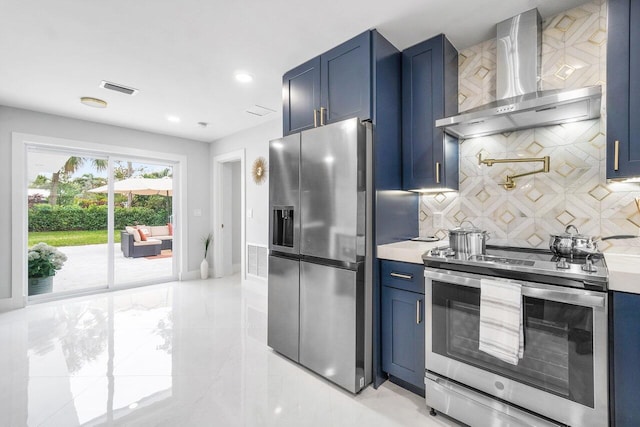 kitchen with wall chimney range hood, blue cabinetry, and appliances with stainless steel finishes