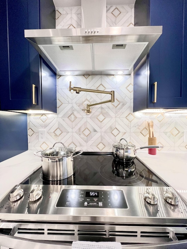 kitchen featuring blue cabinetry, wall chimney exhaust hood, stainless steel electric range oven, and tasteful backsplash