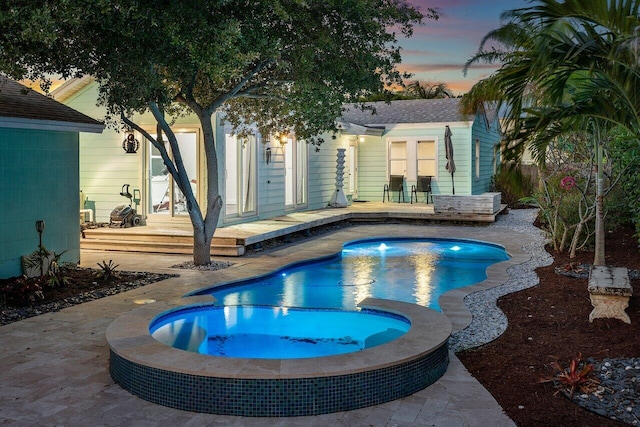 pool at dusk with an in ground hot tub, a patio, and french doors