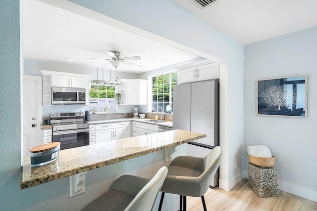 kitchen featuring light hardwood / wood-style floors, white cabinets, kitchen peninsula, stainless steel appliances, and ceiling fan