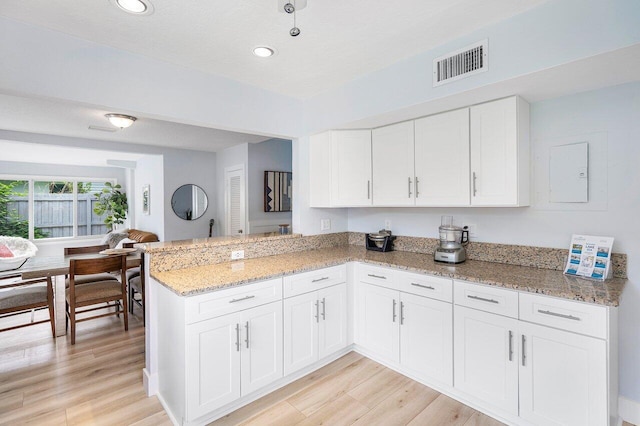 kitchen featuring light hardwood / wood-style floors, a textured ceiling, white cabinets, kitchen peninsula, and light stone countertops