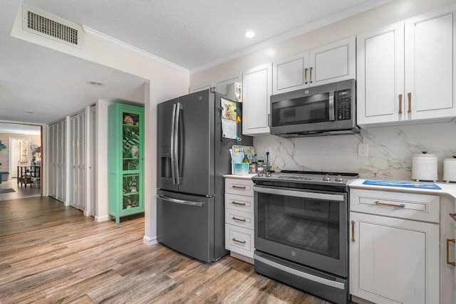 kitchen featuring appliances with stainless steel finishes, crown molding, a textured ceiling, white cabinets, and hardwood / wood-style floors