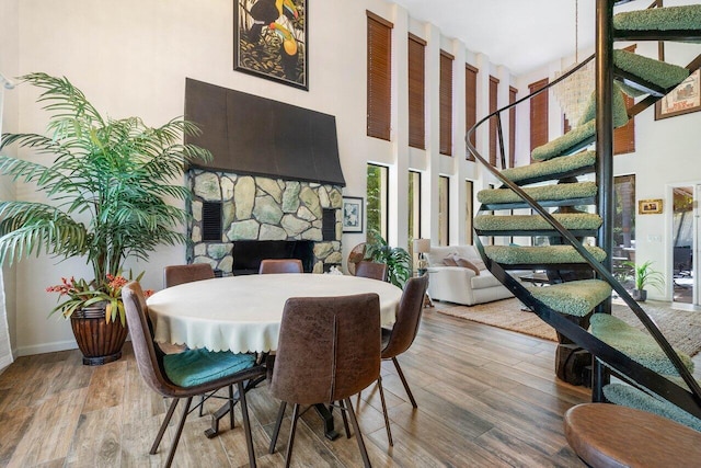 dining area with a stone fireplace, a towering ceiling, and hardwood / wood-style floors