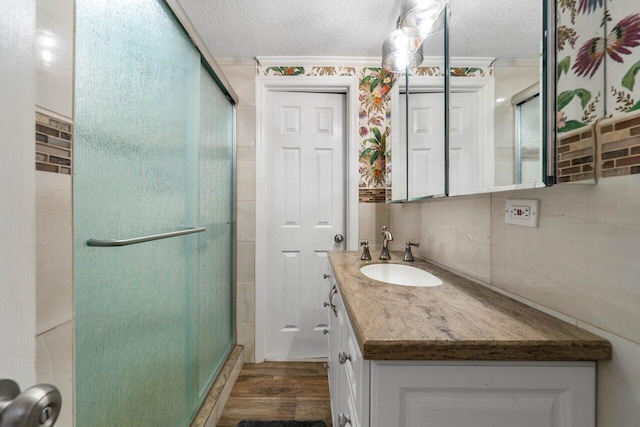 bathroom with vanity with extensive cabinet space, a shower with shower door, hardwood / wood-style floors, and a textured ceiling