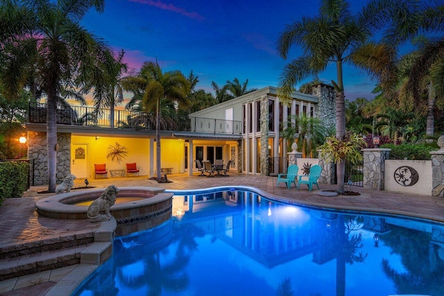 pool at dusk featuring an in ground hot tub and a patio