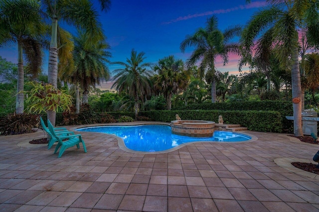 pool at dusk with a patio and an in ground hot tub