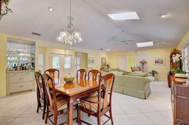 dining area featuring vaulted ceiling with skylight, light tile flooring, and ceiling fan with notable chandelier