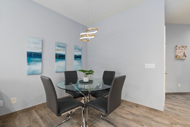 dining area featuring hardwood / wood-style floors, vaulted ceiling, and an inviting chandelier