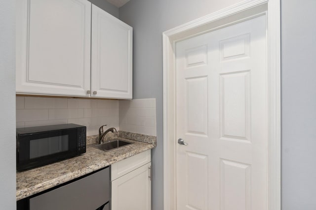 kitchen with backsplash, sink, light stone countertops, and white cabinetry