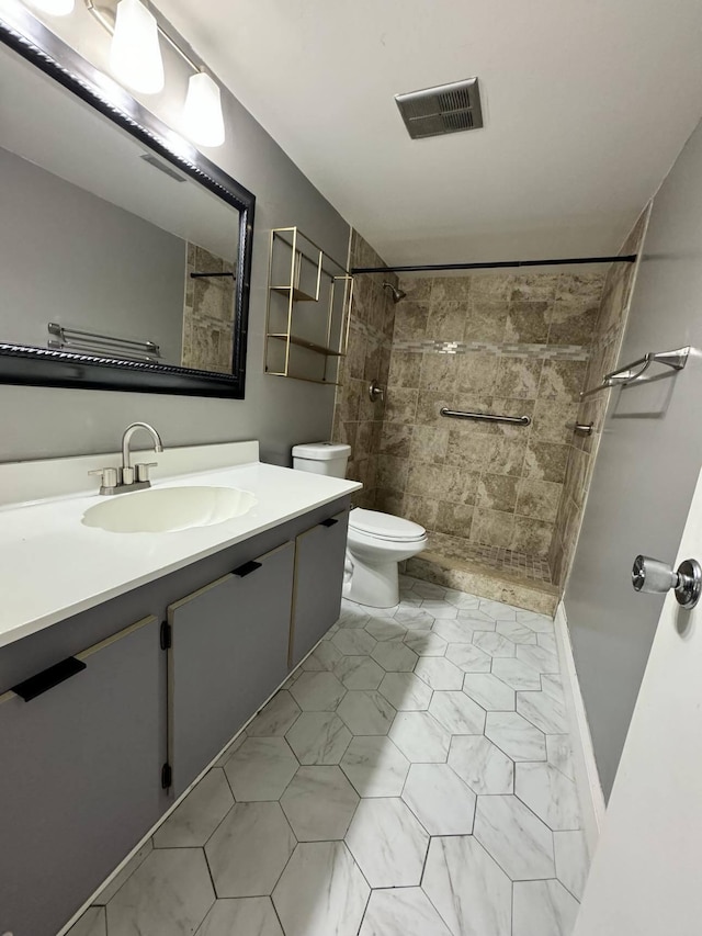 bathroom with vanity, toilet, a tile shower, and tile flooring