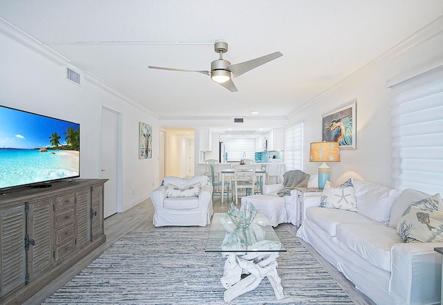 living room with ceiling fan, crown molding, and light wood-type flooring