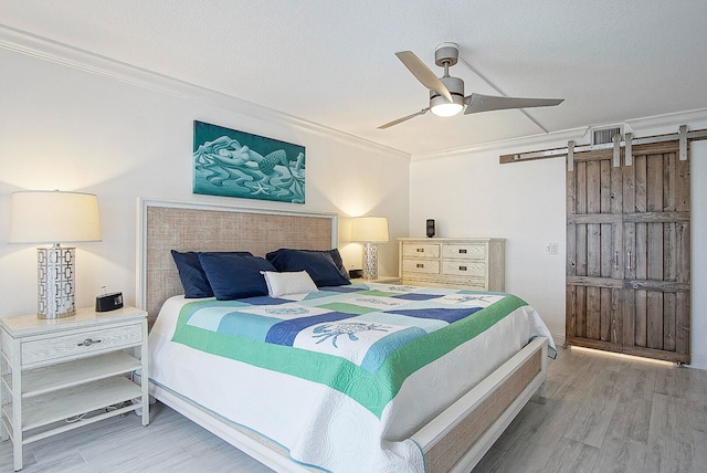 bedroom featuring ornamental molding, a textured ceiling, ceiling fan, a barn door, and hardwood / wood-style floors